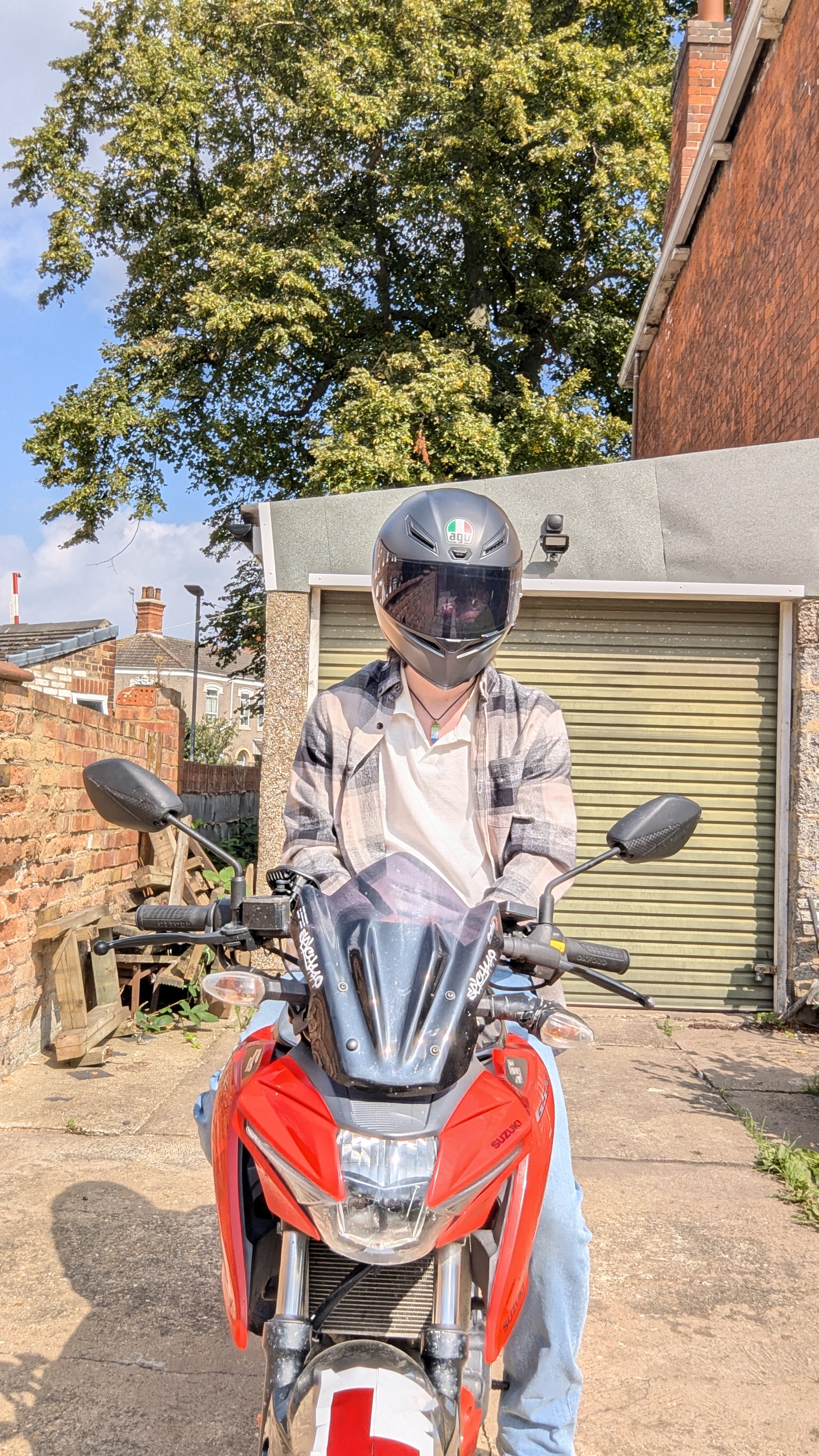 Arthur sitting astride a red motorcycle wearing a casual outfit with a black motorcycle helmet
